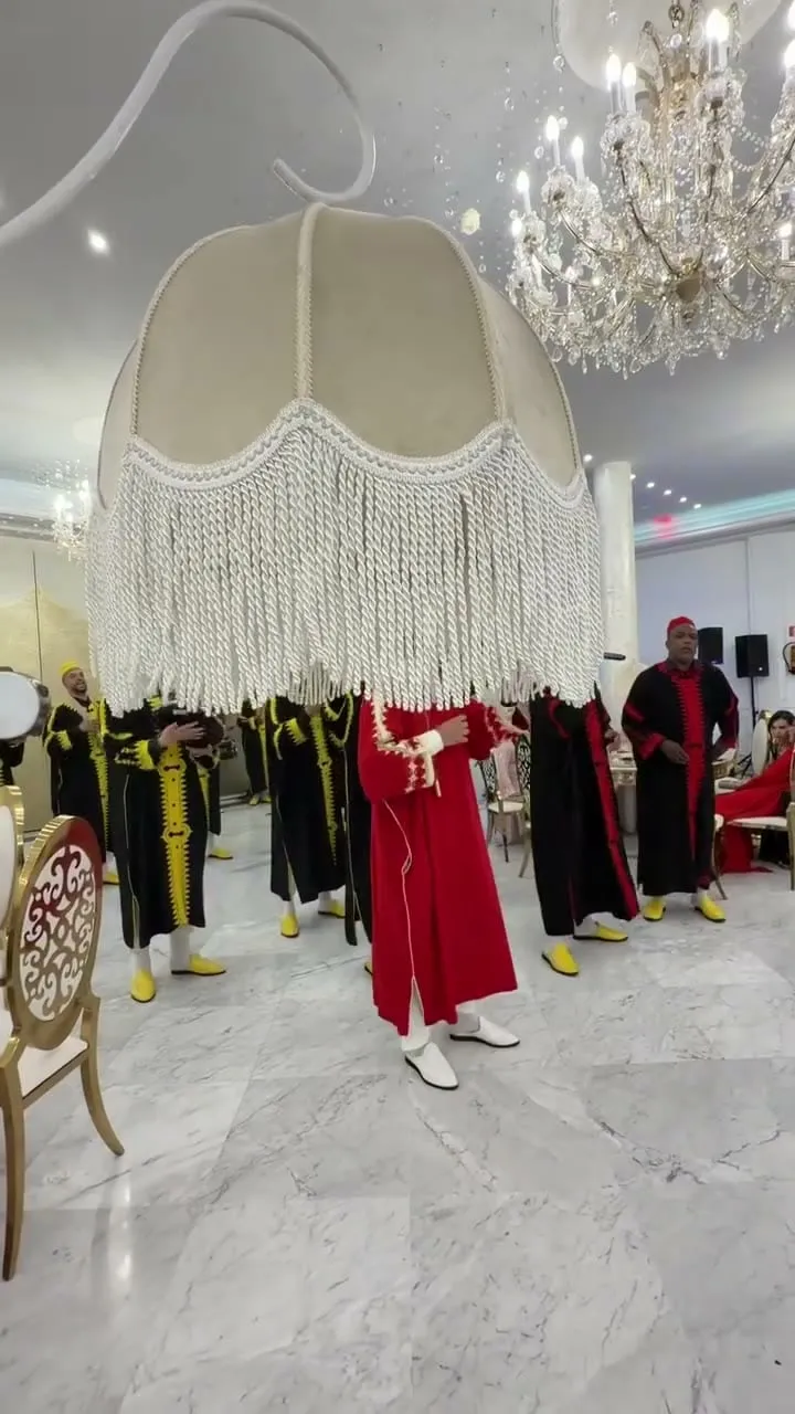 Grupo de dakka marroquí con trajes de terciopelo rojo y dorado en salón con araña de cristal