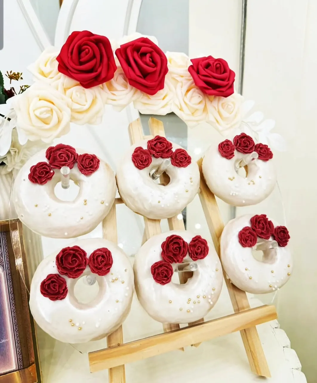 Mini donuts glaseados con rosas rojas sobre soporte blanco y dorado