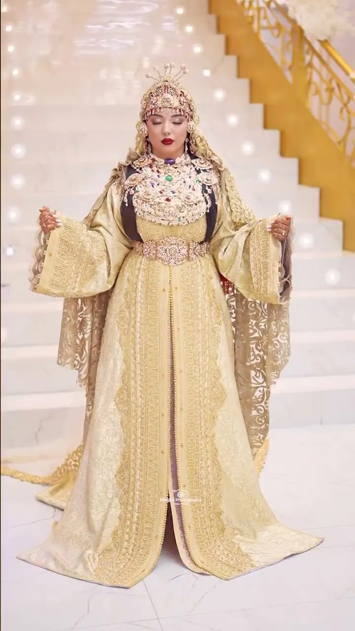 Novia marroquí con caftán dorado bordado en una escalinata de mármol